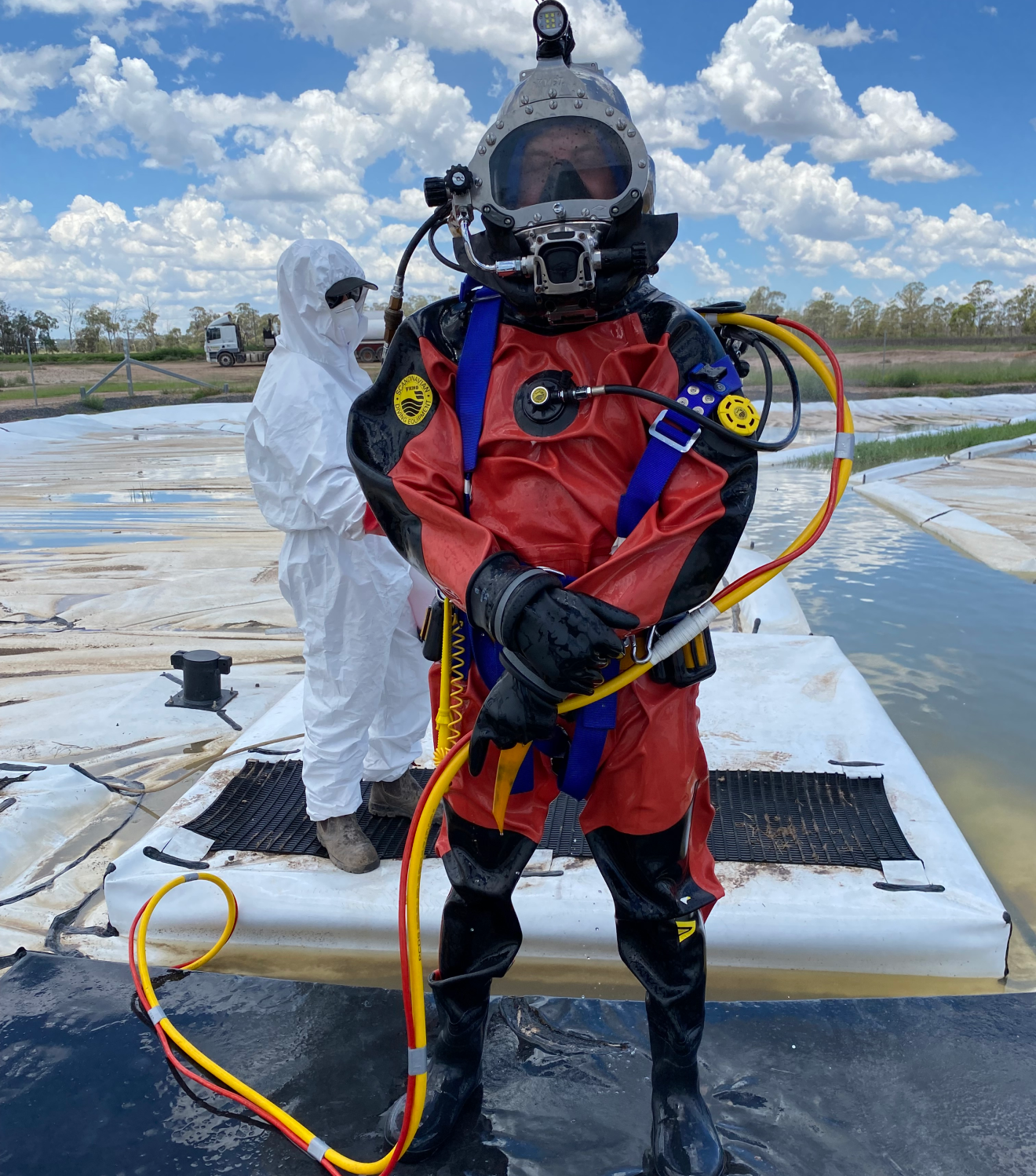 Diver in full gear preparing to put on a helmet near a tank inspection site
