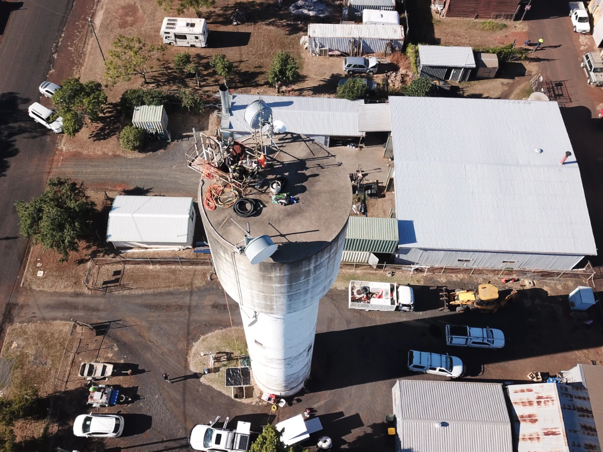 Aerial view of a team conducting maintenance on a tall water tank surrounded by buildings and vehicles, part of a Fire Tanks Australia project.