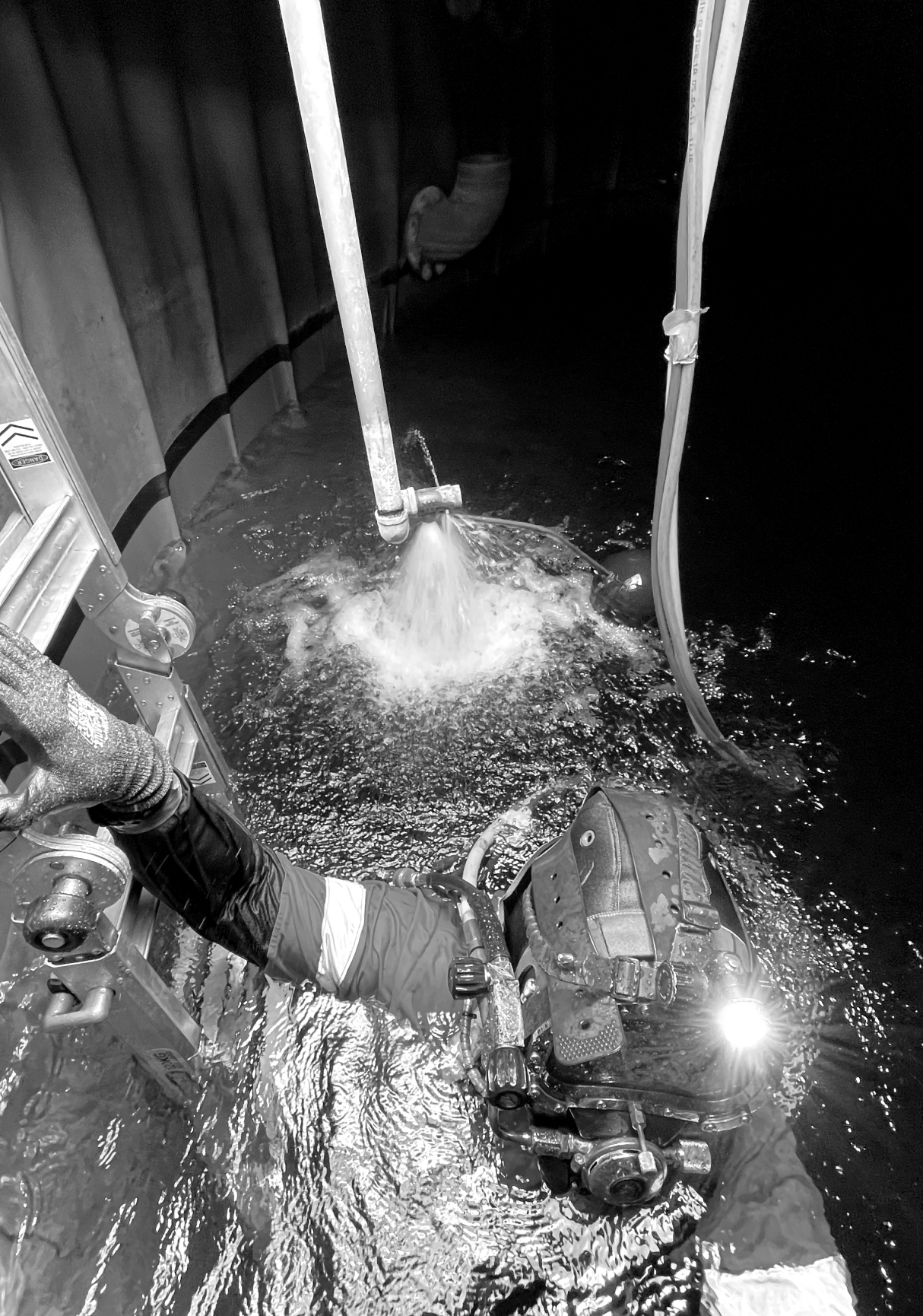 Fire Tanks Australia diver working underwater, adjusting a pipe releasing water, with a black and white image showing the diver in full gear and a ladder in the background.