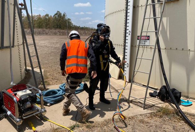 Fire Tanks Australia diver in full gear preparing to enter an underground fire tank with the assistance of a technician and safety hoist system.