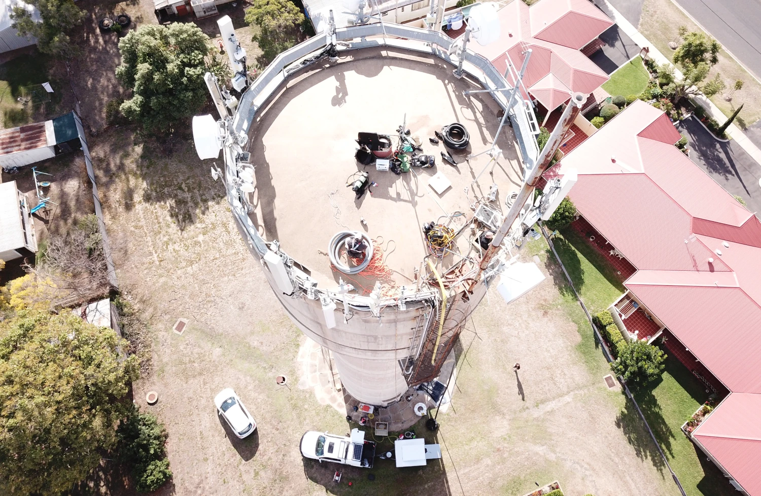 Aerial view of workers on top of a large water tank, surrounded by houses with red rooftops and a clear sky.