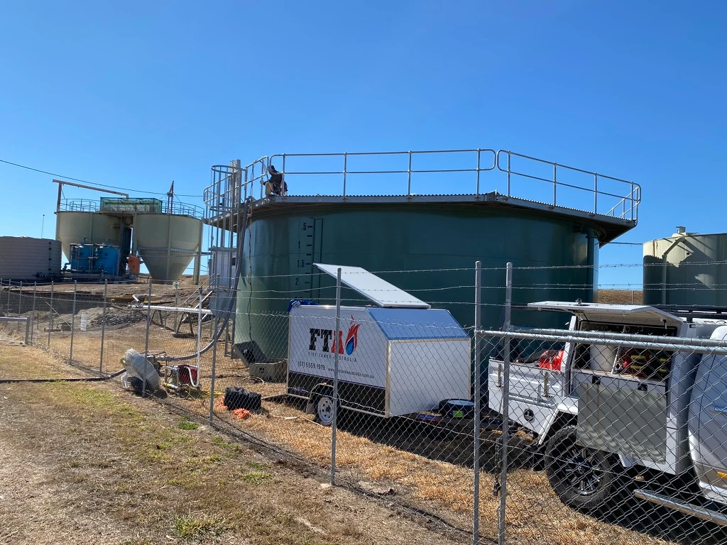 Fire Tanks Australia equipment and vehicles stationed near a large green water tank undergoing maintenance, with additional tanks visible in the background on a clear day.