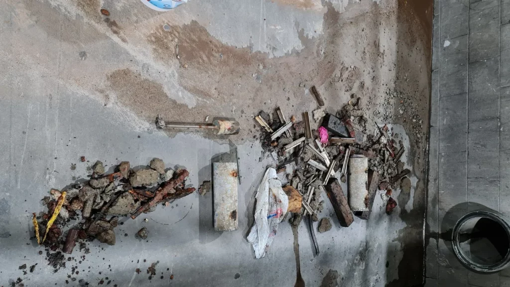 Collection of debris including metal rods, concrete, and other materials found in a confined space.