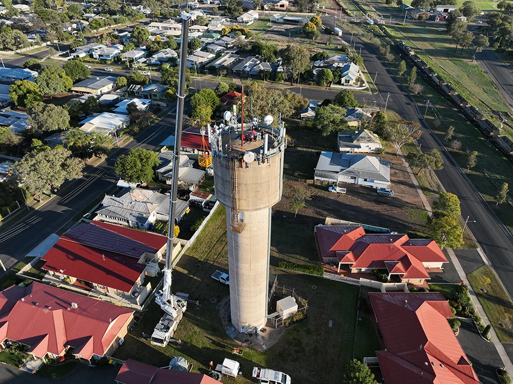 Aerial view of Fire Tanks Australia performing maintenance on a tall water tower in a residential area.