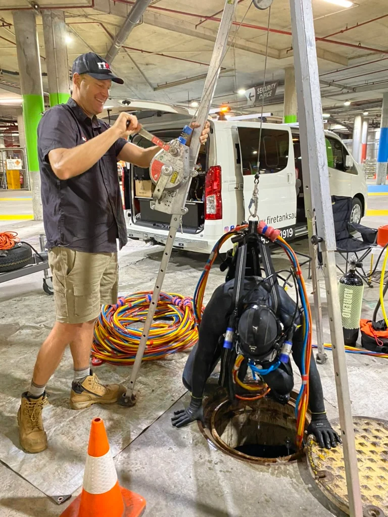 Fire Tanks Australia team using a safety hoist system to lower a diver into an underground fire tank for inspection.