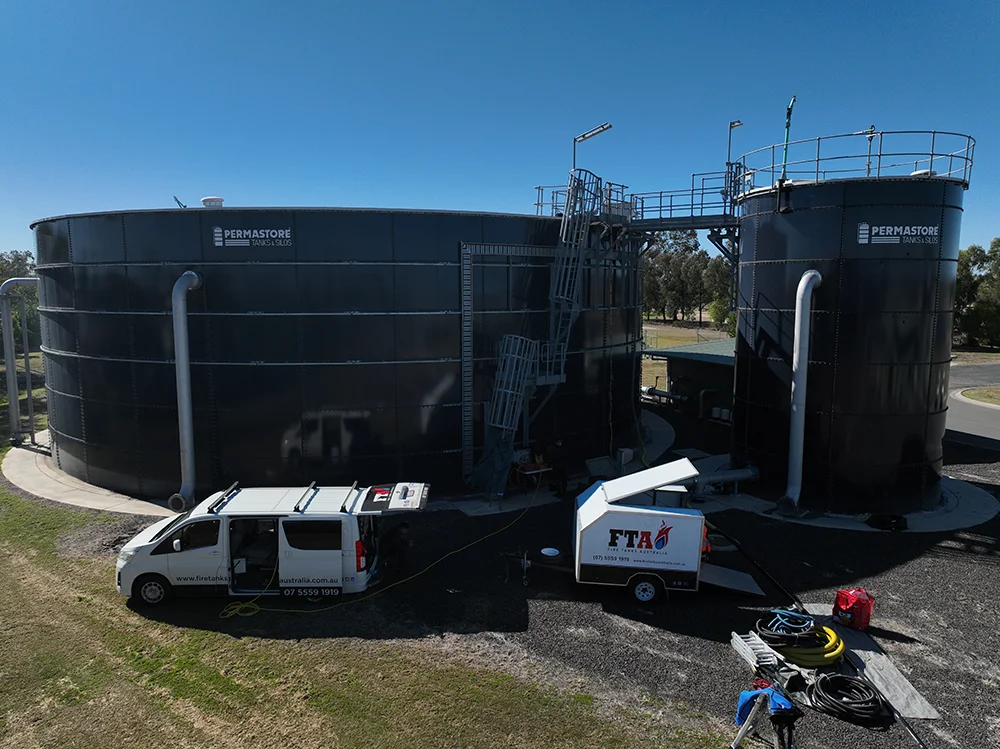 Fire Tanks Australia conducting maintenance on large Permastore fire tanks with professional equipment and vehicles on-site.