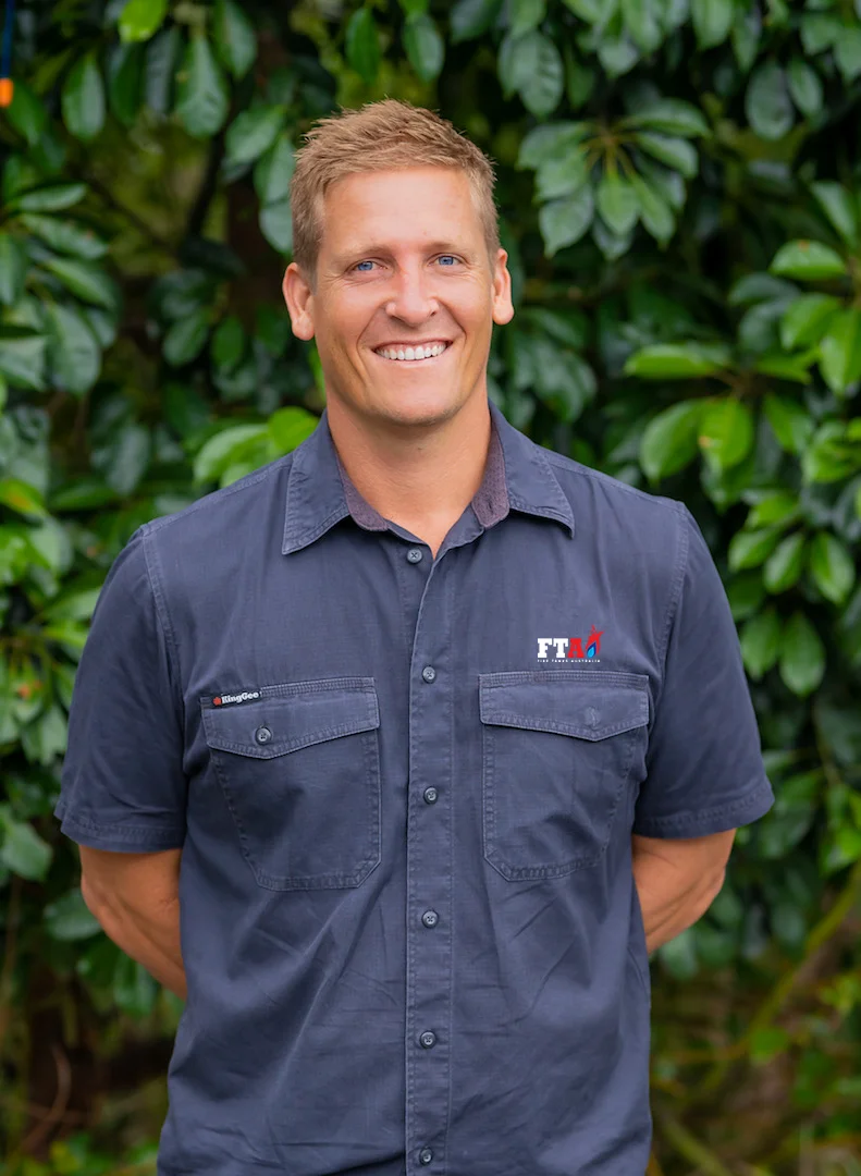 Sam from Fire Tanks Australia smiling, wearing an FTA-branded shirt, standing in front of a leafy green background.