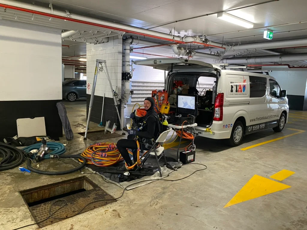 Technician from Fire Tanks Australia seated with inspection equipment beside a parked van in an underground carpark, preparing for a tank inspection.