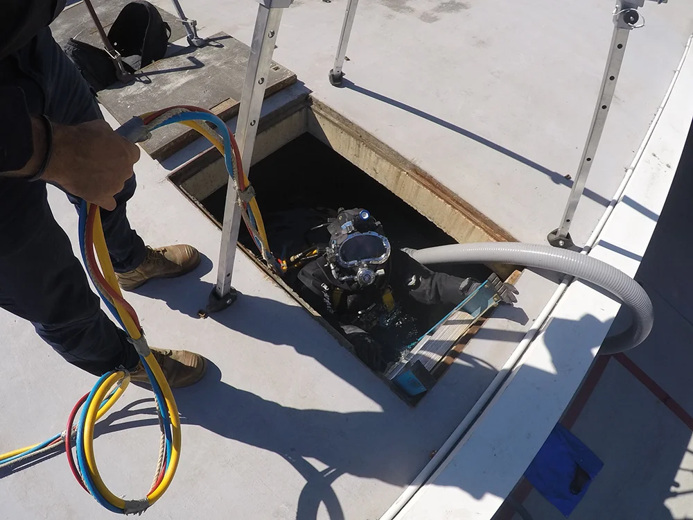 Fire Tanks Australia diver emerging from an underground fire tank during a maintenance operation, assisted by a technician with safety equipment.