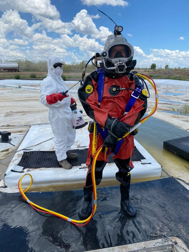 Fire Tanks Australia diver in specialized contamination suit with safety equipment, assisted by a technician in protective gear during a fire tank inspection.