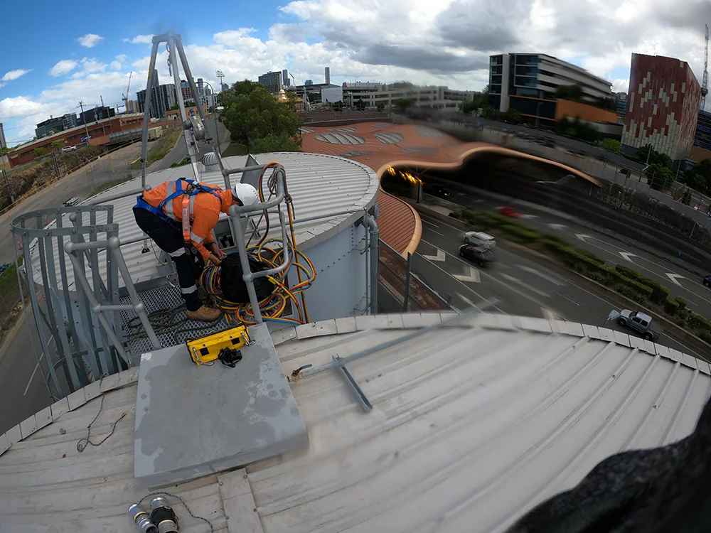 Technician securing equipment on top of a water tank overlooking a busy urban roadway with cityscape in the background.