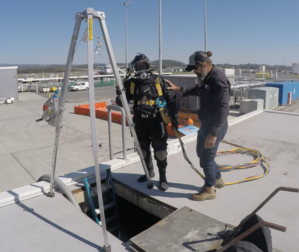Fire Tanks Australia diver in full gear preparing to enter an underground fire tank with the assistance of a technician and safety hoist system.