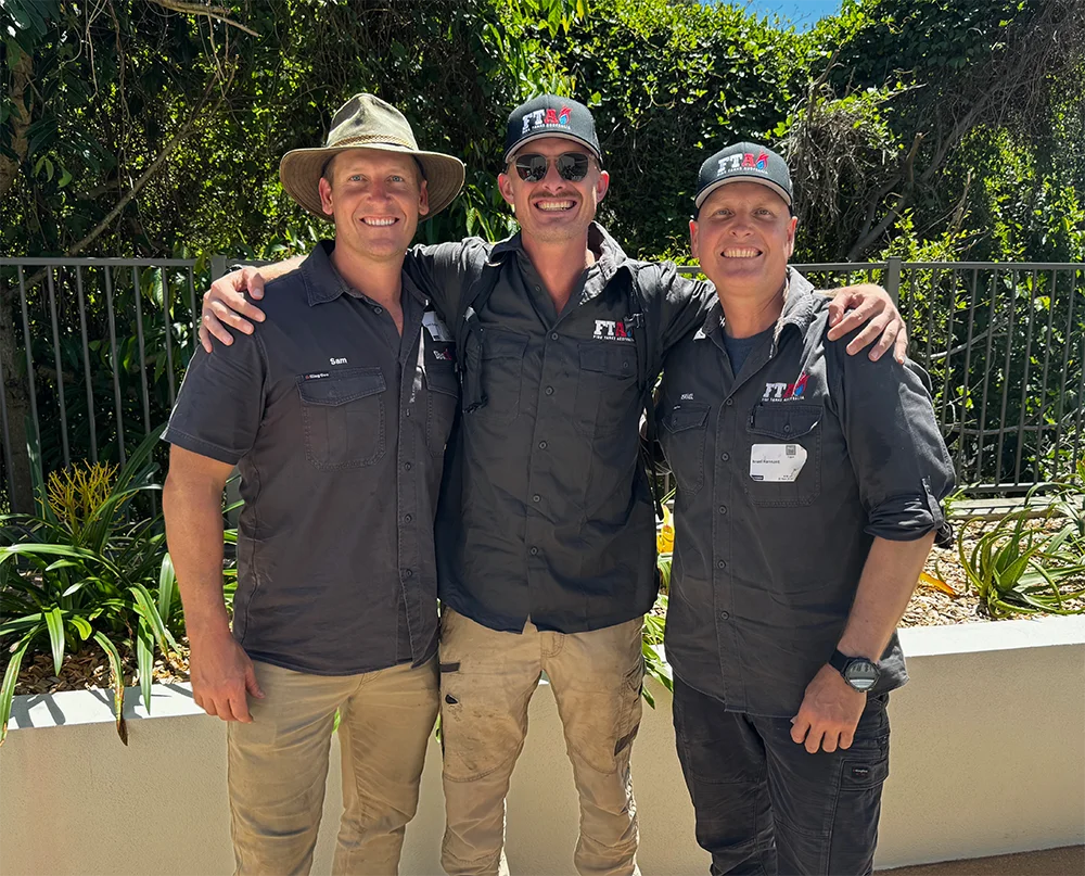 Three Fire Tanks Australia team experts standing together outdoors, wearing branded uniforms and smiling.